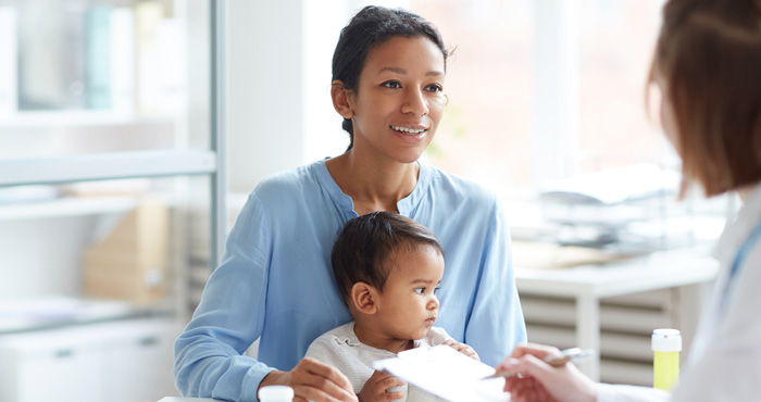 Photo: Mother holding her child in a clinic setting speaking with a clinician.